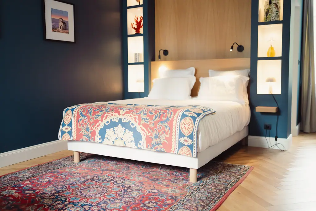 Le lit, son jeté aux motifs rouges et bleus, le tapis persan et le mur bleu canard