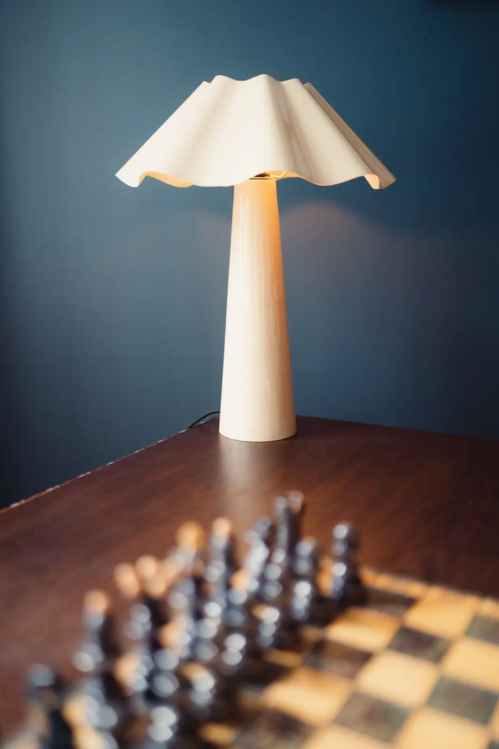 La lampe en papier plissé allumée sur le mur bleu, un jeu d'échecs au premier plan