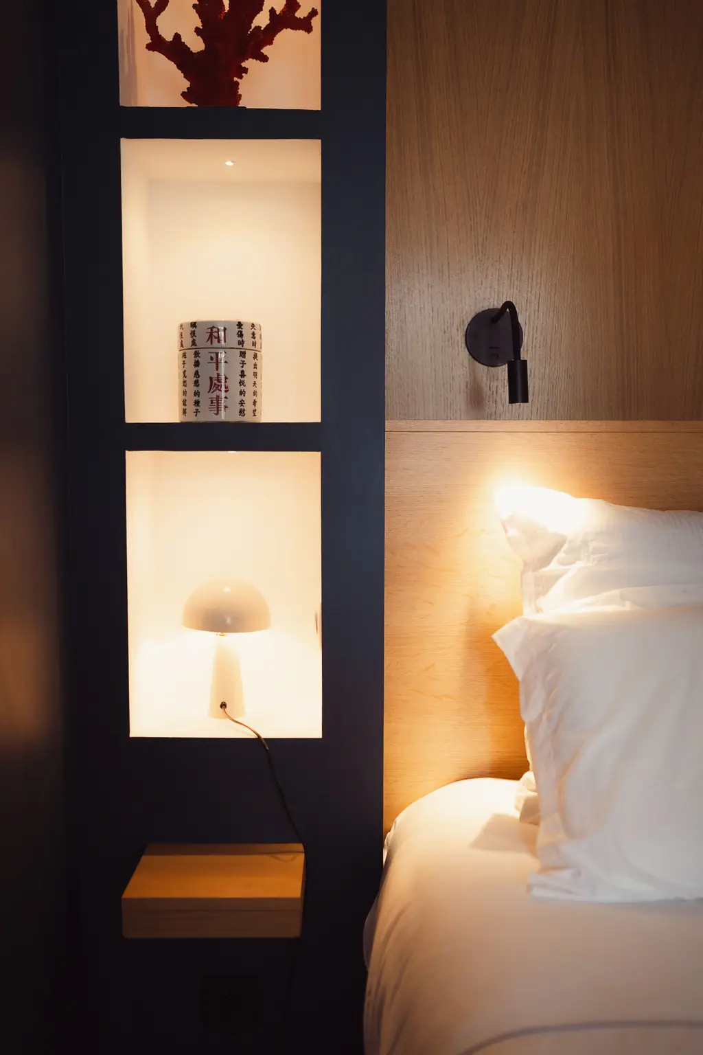 Une niche éclairée à côté du lit, un livre et une petite lampe