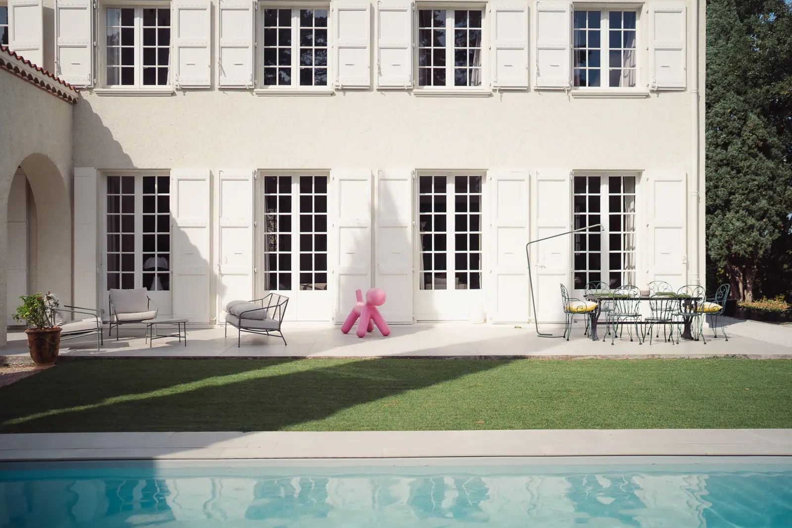 La façade blanche de la maison, ses volets ouverts et son reflet dans la piscine
